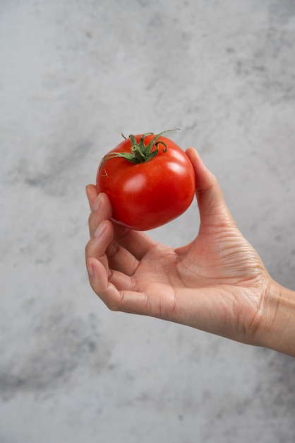 Hand holding a fresh red tomato on a marble background.