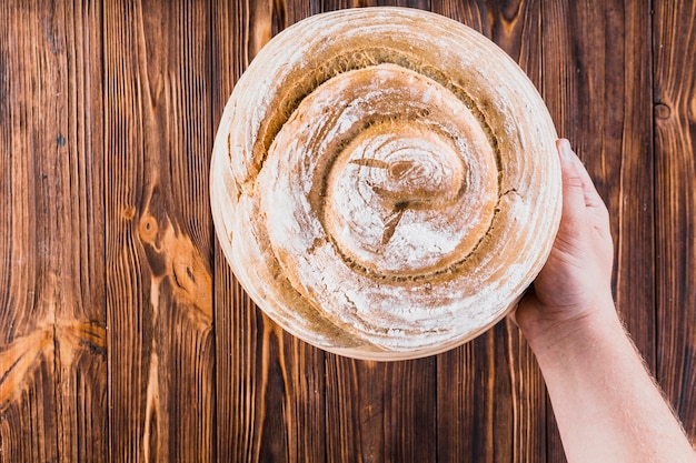 Free photo hand holding freshly baked swirl bread on wooden background