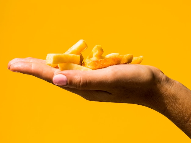 Hand holding fries on yellow background