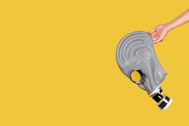 Hand holding gas mask on yellow background