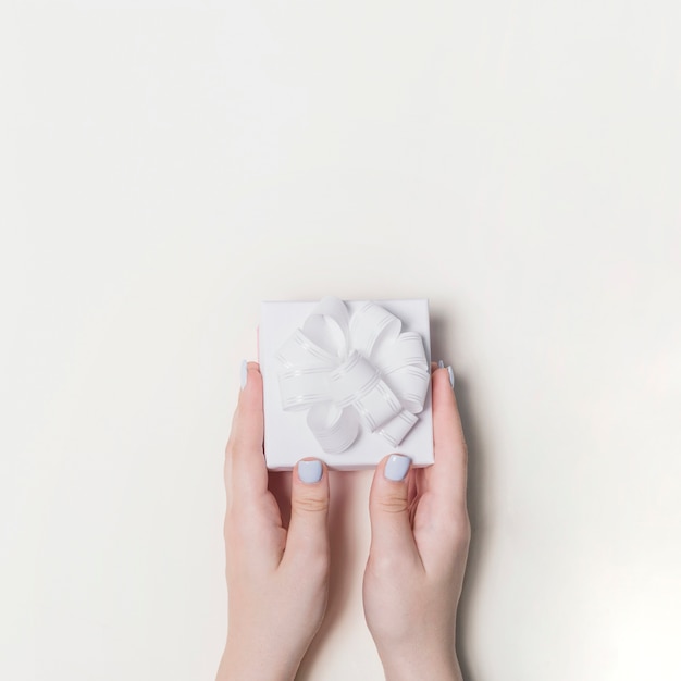 Hand holding gift box decorated with white ribbon on blank background