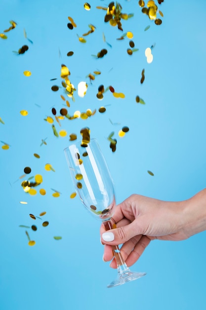 Hand holding a glass surrounded by golden sequins and confetti