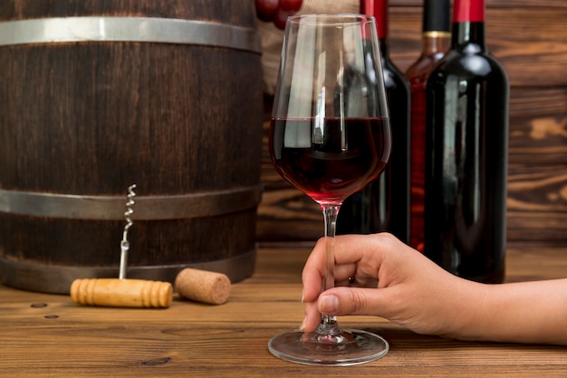 Hand holding glass of wine with bottles and barre