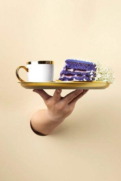 Hand holding golden plate with cake and mug