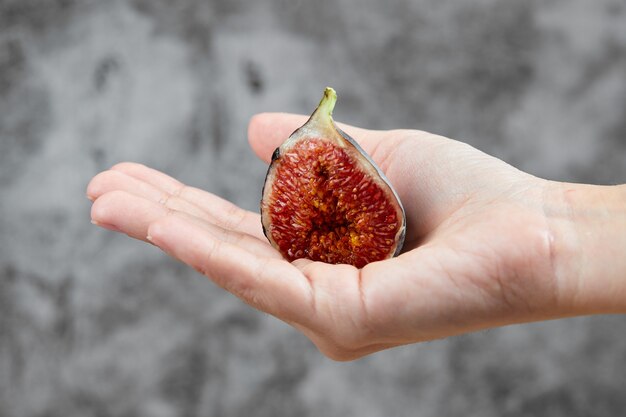 Hand holding a half slice of fig on marble.