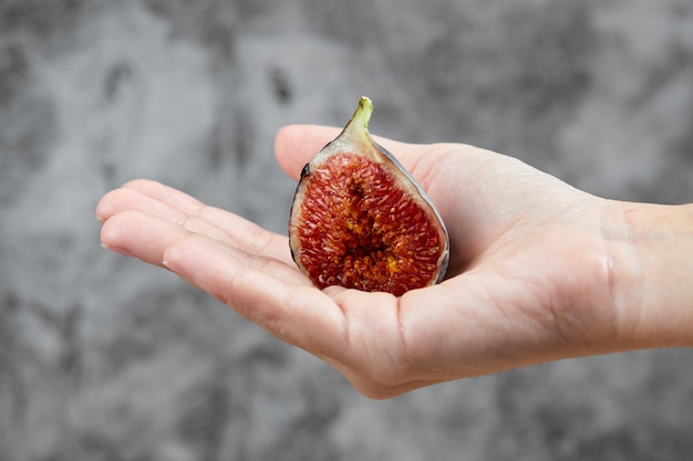 Hand holding a half slice of fig on marble.