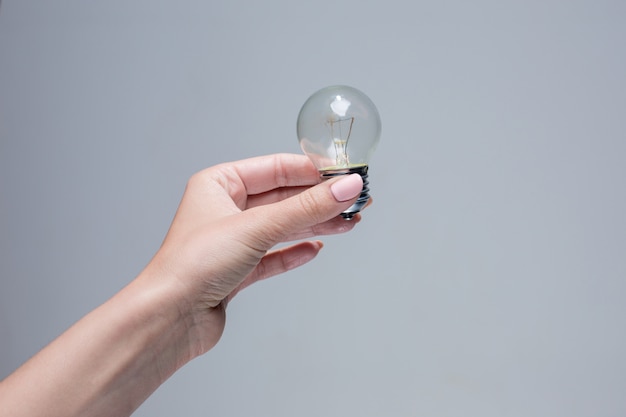 Hand holding an incandescent light bulb on gray space