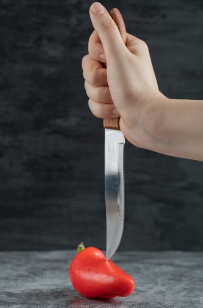 Hand holding a knife and red pepper .