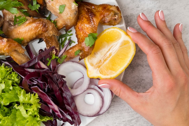 hand holding a lemon close to chicken wings