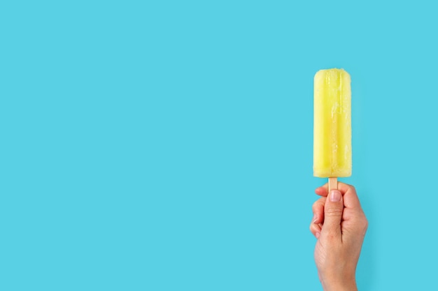 Hand holding a lemon popsicle on blue background