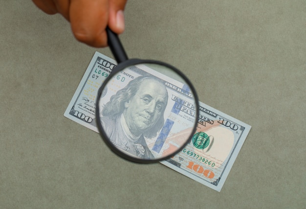 hand holding magnifying glass over banknote.