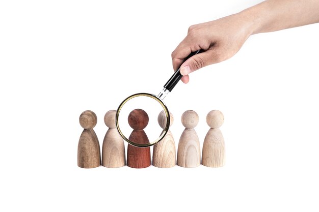 Hand holding a magnifying glass over a red figurine in a row