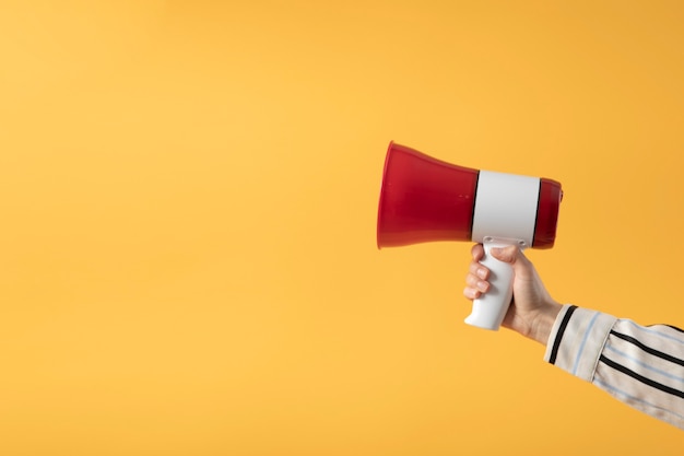 Hand holding megaphone with yellow background