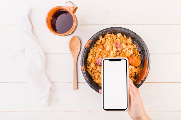 Hand holding mobile on table with dish