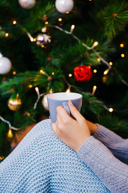 Hand holding mug in front of christmas tree