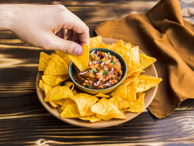 Hand holding nacho in cup of garnish