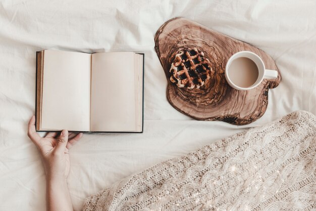 Hand holding notebook near cookie and hot drink on wooden stand