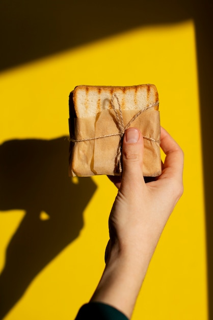 Free photo hand holding  paper-wrapped sandwich