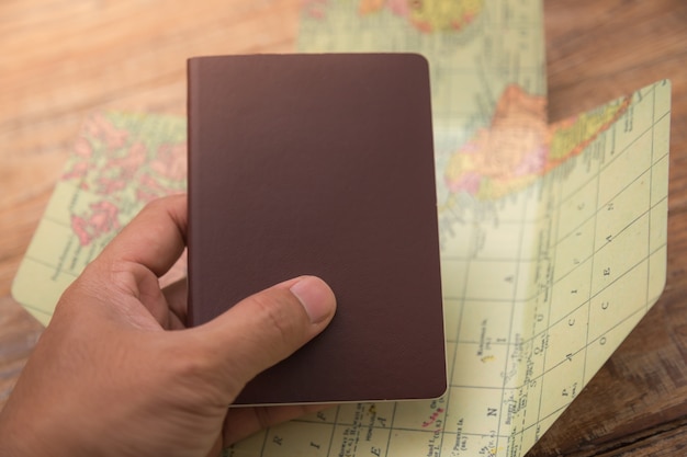 Hand holding a passport with a map of the world behind