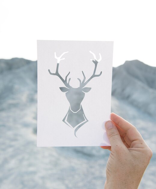 Hand holding perforated paper moose art with mountain background