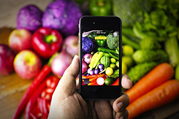 Hand holding a phone and photographing vegetables