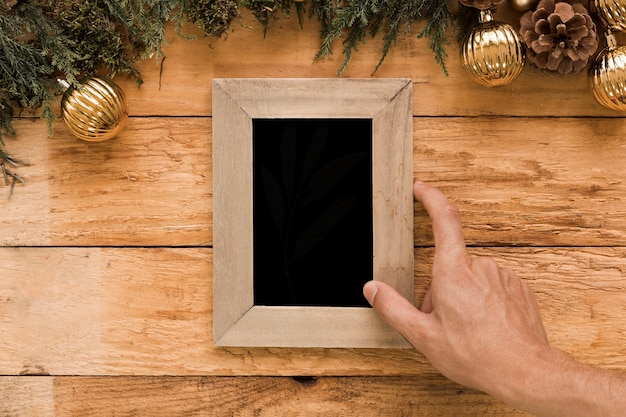 Hand holding photo frame near coniferous twigs and Christmas balls 