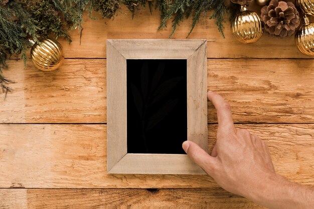 Hand holding photo frame near coniferous twigs and Christmas balls 