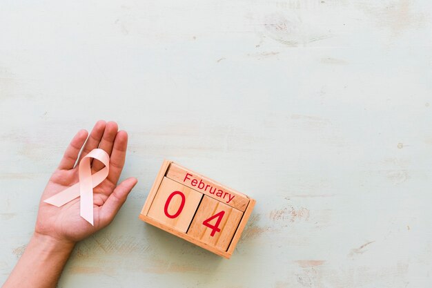 Hand holding pink awareness ribbon and 4th February wooden box on backdrop