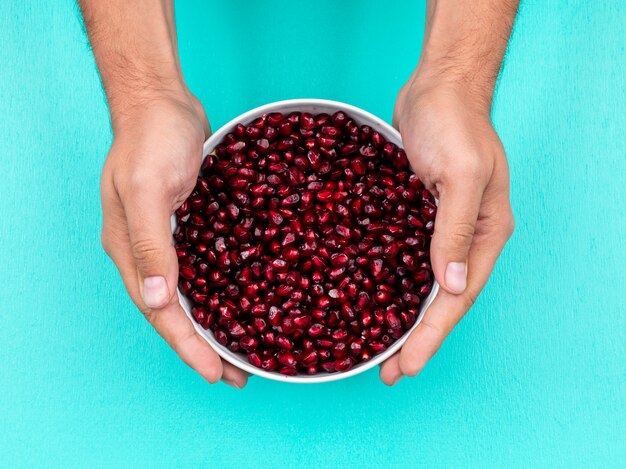 Hand holding pomegranate in plate top view on light blue surface