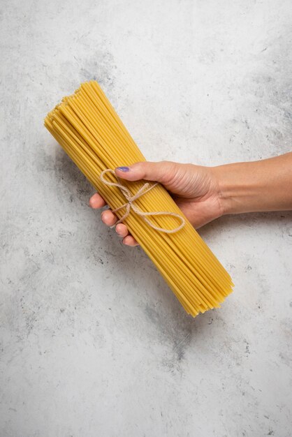 Hand holding raw spaghetti on white surface.