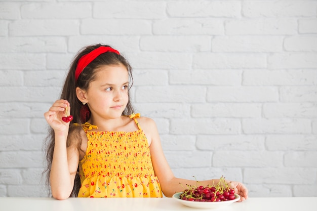 Hand holding red cherries in front of brick wall