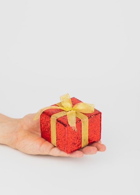 Hand holding red gift box with golden ribbon