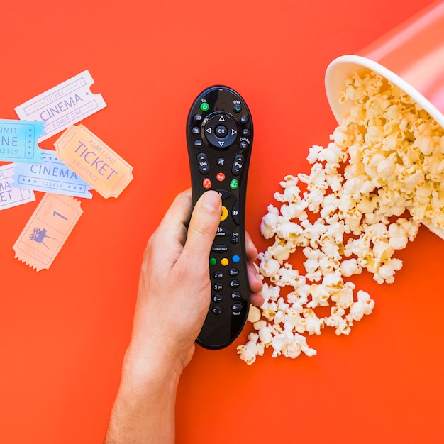 Mano che tiene telecomando su popcorn e biglietti per il cinema