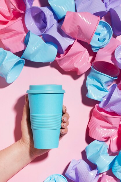 Hand holding reusable cup next to plastic cups