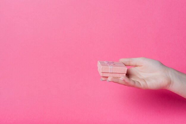 Hand holding small gift box on pink background