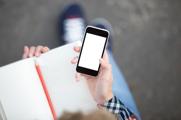 Hand holding a smartphone against a copybook with a pencil