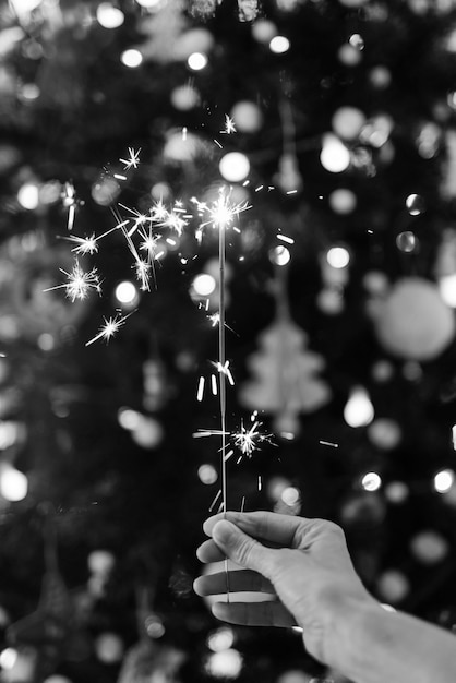 Hand holding a sparkler with a Christmas tree in black and white