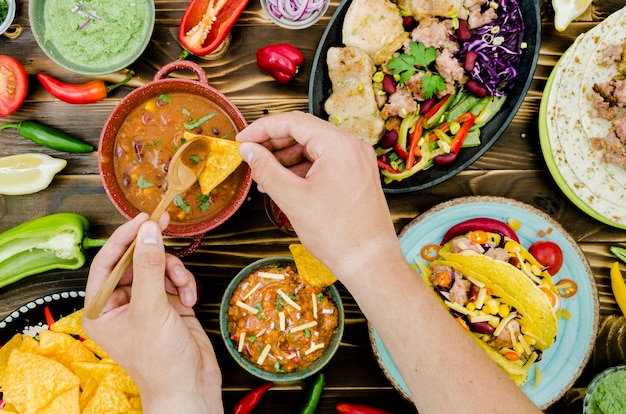 Hand holding spoon and nacho near Mexican food