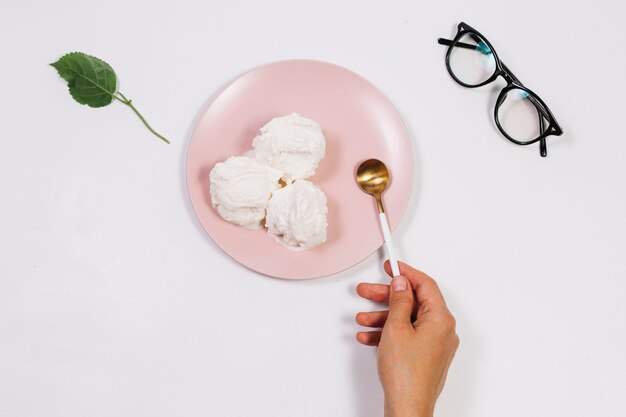 Hand holding spoon near ice cream on plate 