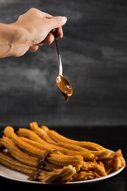 Hand holding a spoon with chocolate above churros