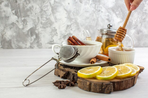 Hand holding spoon with honey black tea in a white cup on white table