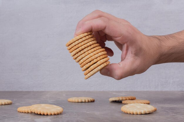 Hand holding stack of biscuits on marble table.