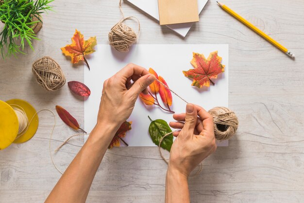 Hand holding string with fake autumn leaves on white paper over the textured backdrop