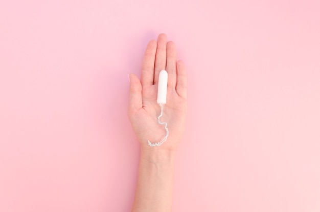 Hand holding tampon on pink background