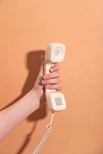 Free photo hand holding telephone with orange background