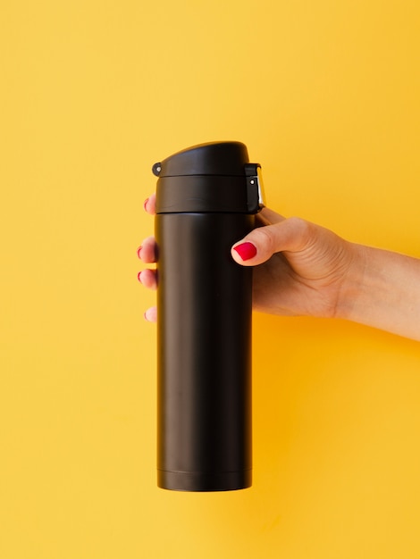Free photo hand holding thermos mock-up on yellow background