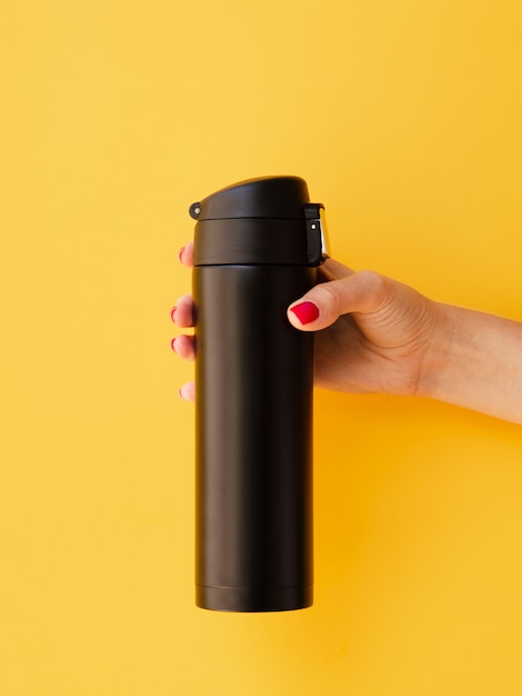 Hand holding thermos mock-up on yellow background