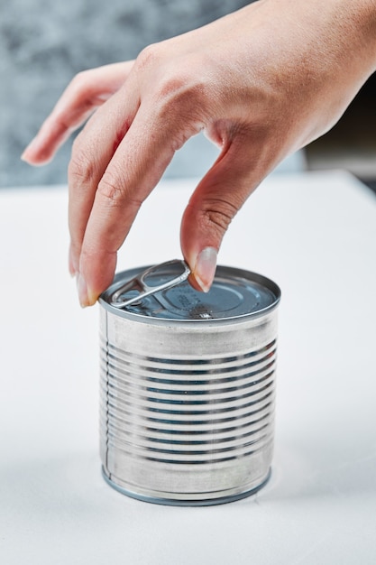 Hand holding a tin with boiled green peas on a white table.