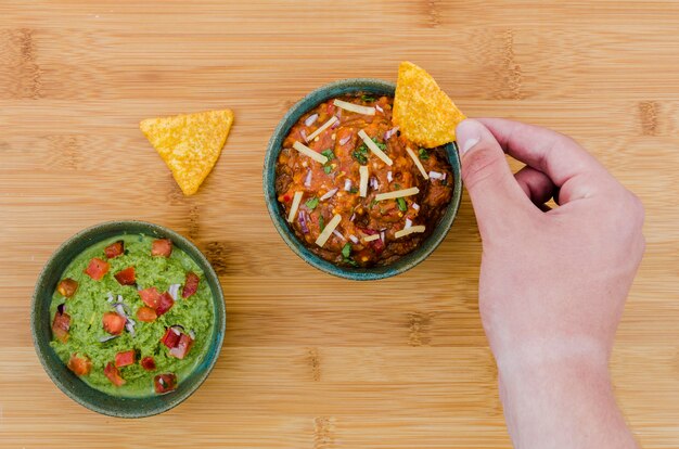 Hand holding triangular snack near cup of garnish