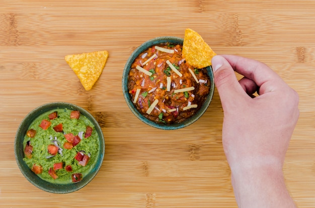 Hand holding triangular snack near cup of garnish